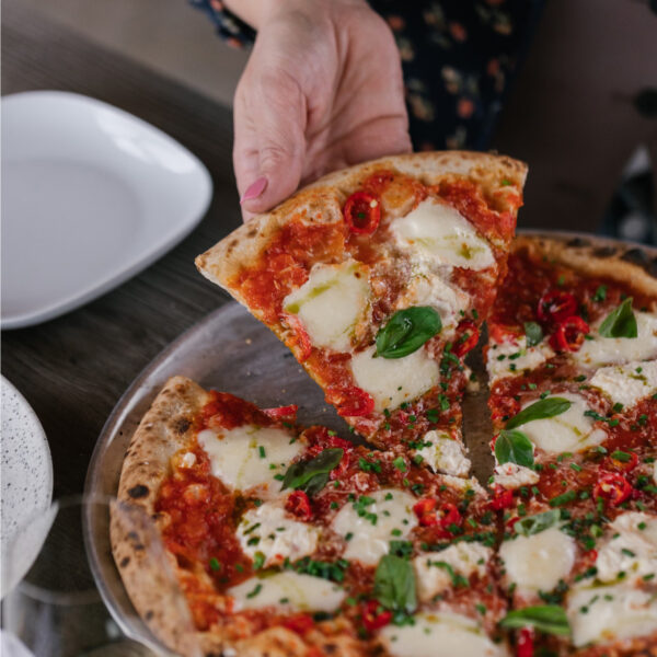hand taking slice of pizza from tray
